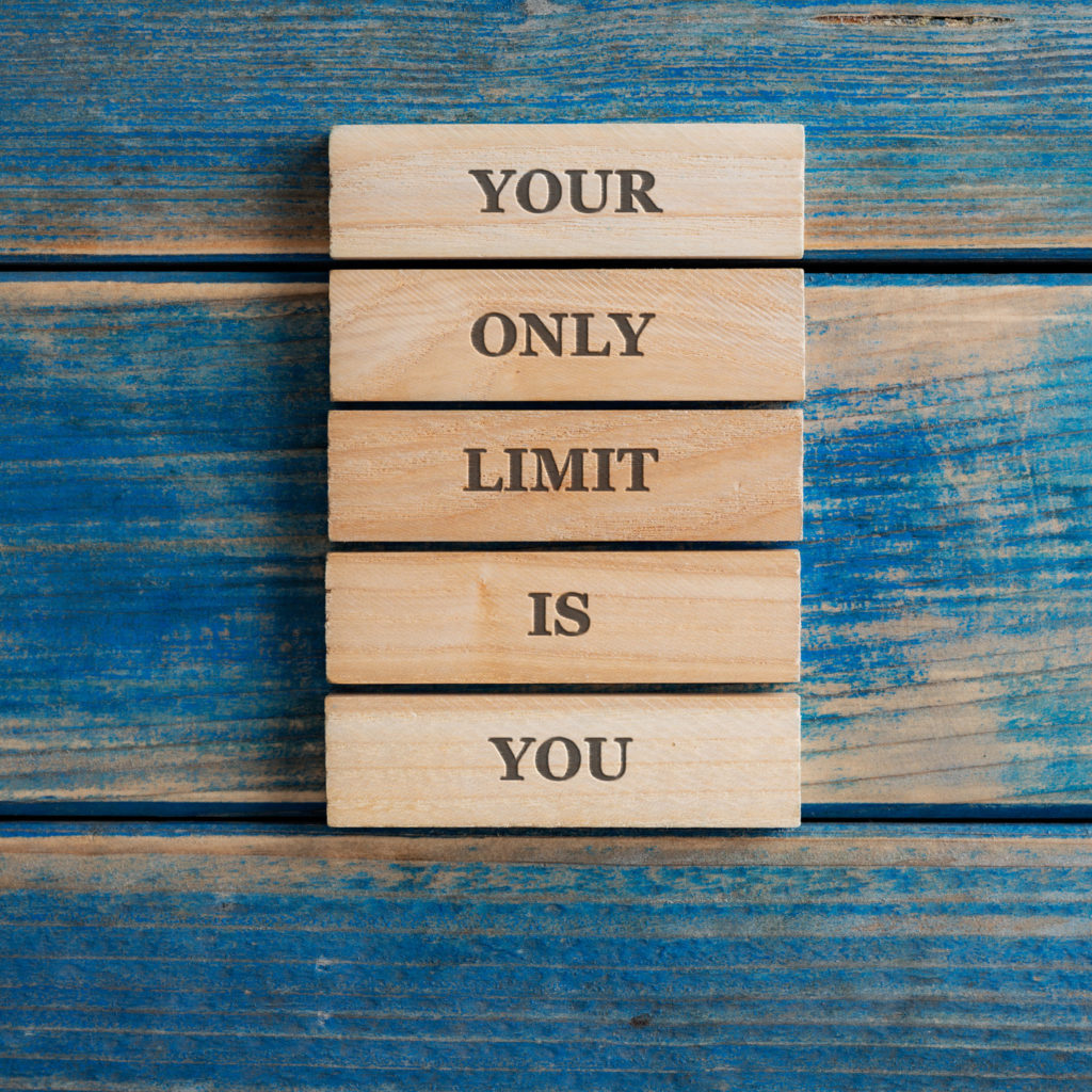 Your only limit is you sign written on a stack of five wooden pegs placed on tetured blue wooden background.