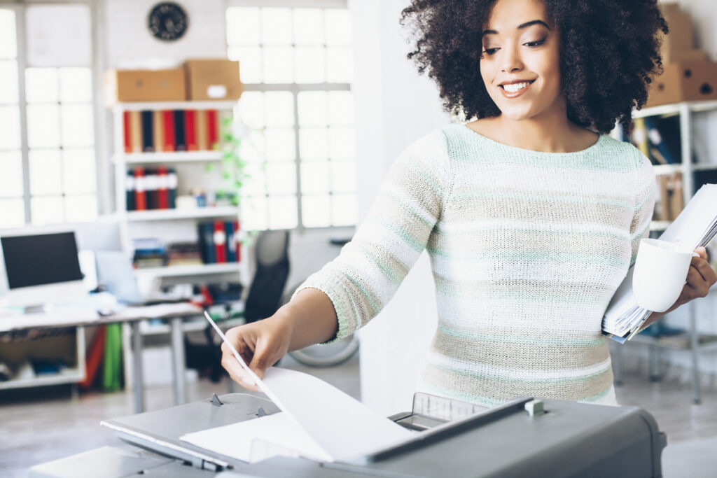 Smiling female assistant using copy machine at work Business Coach for Interior Designers